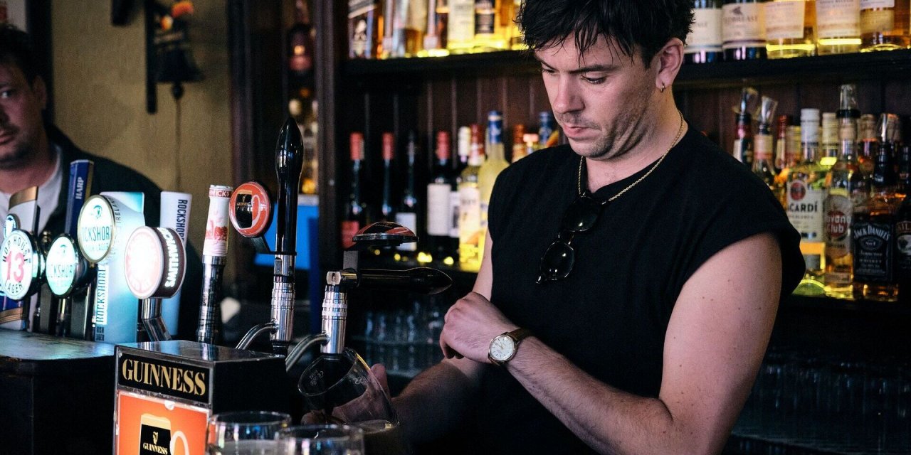 male bartender wearing black pouring a pint behind the bar